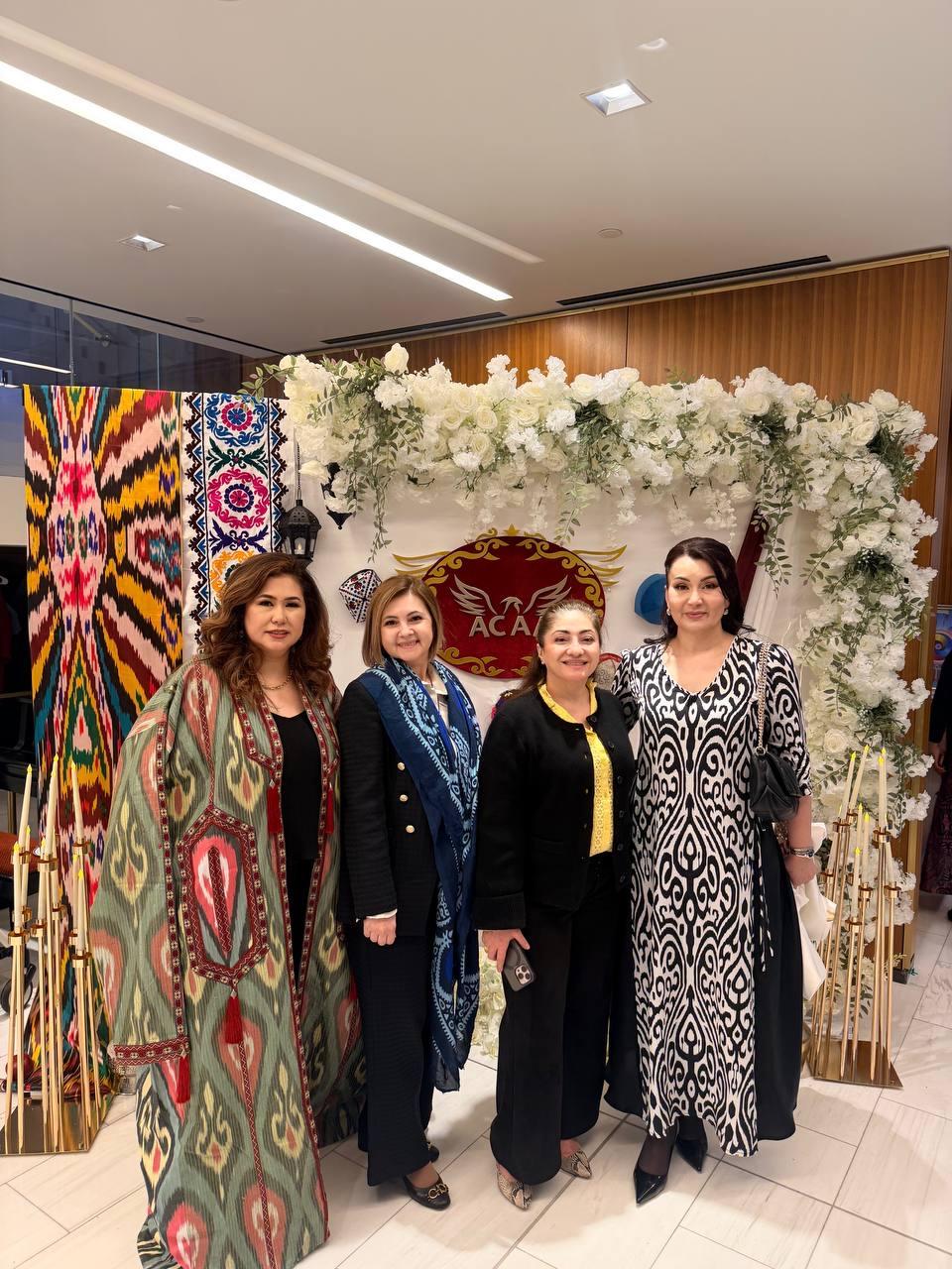 Four women in traditional and formal dress before a white floral arch
