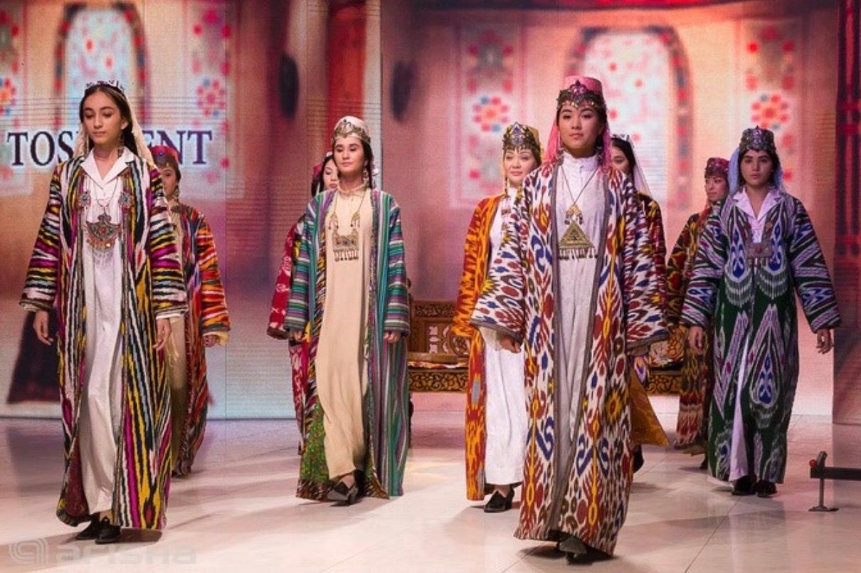 Models in ikat gowns and traditional jewelry walking a runway during a fashion showcase